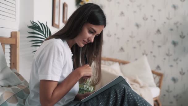 Jonge vrouw zit op bed en schrijft ochtendbladzijden in dagboek, slow motion. — Stockvideo