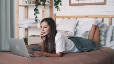 Güzel kız freelancer dizüstü bilgisayar ve telefonla aramalar ile yatakta yatıyor, yavaş hareket
