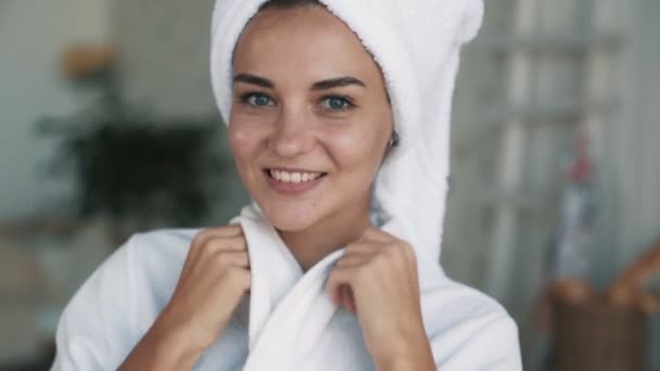 Ritratto di ragazza in accappatoio, con asciugamano sulla testa guarda nella macchina fotografica, sorride, rallentatore — Video Stock