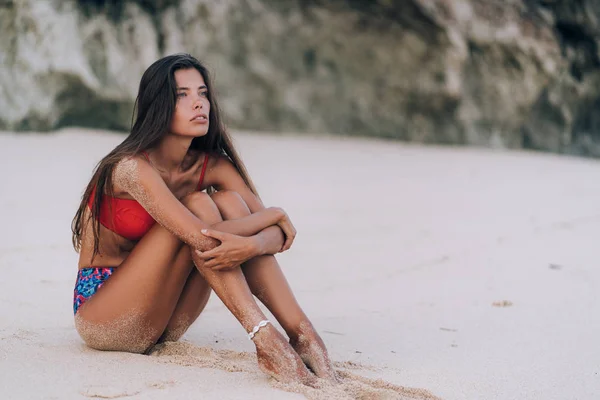 Sottile donna abbronzata in costume da bagno colorato si rilassa sulla spiaggia con sabbia bianca — Foto Stock