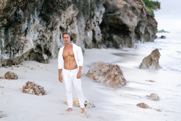 섹시한 무두질 남자 에 흰색 셔츠, 바지 는 해변에 달려, 배경에 바다 파도 — 스톡 사진