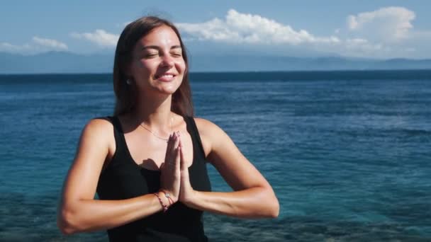 Retrato de hermosa chica sonriente medita con los ojos cerrados, océano en el fondo — Vídeos de Stock