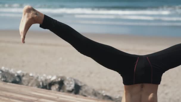 Nahaufnahme Beine des Mannes beim Yoga im Kopfstand Hintergrund des Ozeans. — Stockvideo