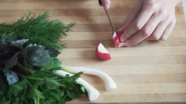 Fermez les mains de la femme avec un couteau tranchant des radis sur une planche en bois, au ralenti — Video