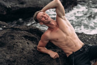 Siyah pantalonunda seksi Fitness erkek modeli ve siyah kumlu plajda çıplak poz.