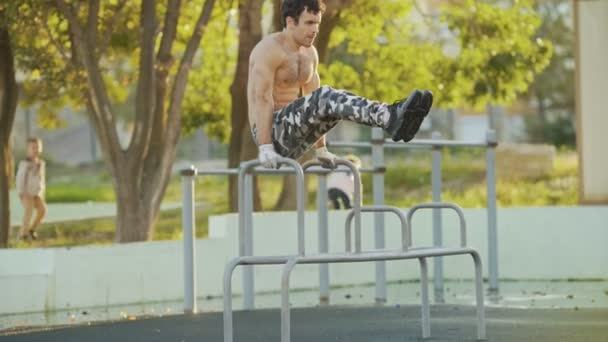 Mladý atletický muž bez trička dělá cvičení na paralelních tyčích v rekreačním parku — Stock video