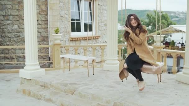 Aantrekkelijk meisje in beige vacht rijden op swing en genieten van de tijd alleen — Stockvideo