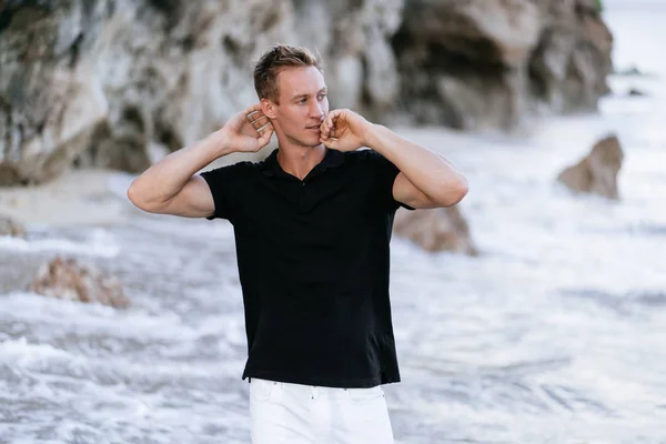 섹시한 근육질의 남자 에 검정 폴로 셔츠 휴식 에 바닷가, 파도 에 배경 — 스톡 사진