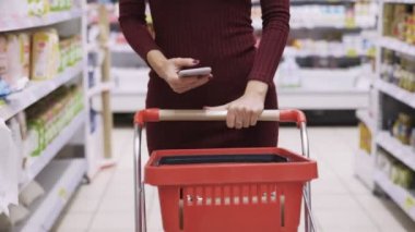 Close-up kadın elleri süpermarket ticaret katında kırmızı sepeti rulo ve telefon kullanımı