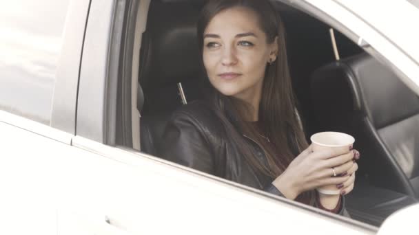 Молодая женщина, сидя в машине и держа в руках кофе, закрывает окно машины — стоковое видео