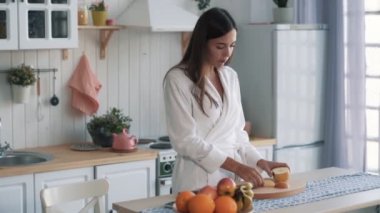 Beyaz bornozkız mutfakta dilimlenmiş elma yiyor, pencereden dışarı bakıyor, yavaş hareket