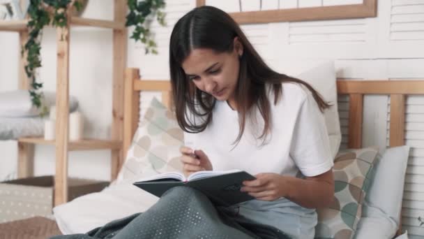 Mladá žena sedí na posteli a píše ranní stránky do deníku, zpomaleně. — Stock video