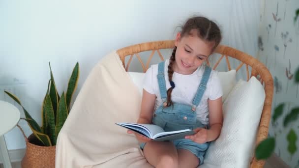 La niña se sienta en el sillón, sostiene el diario y dice algo, cámara lenta — Vídeo de stock