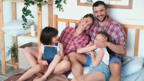 Pais felizes e duas filhas se divertem juntas em casa, se sentam na cama — Vídeo de Stock