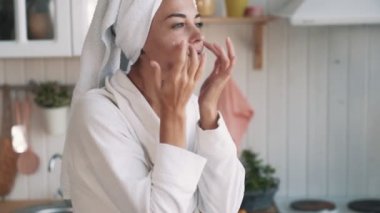 Yakın yukarı, kafa havlu ile kadın yüzünde nemlendirici krem uygular, yavaş hareket
