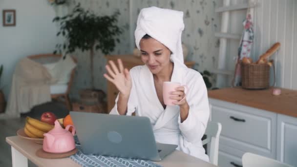 頭にタオルを持つ白いバスローブの女の子は、ラップトップ上のビデオチャット、スローモーションを持っています — ストック動画