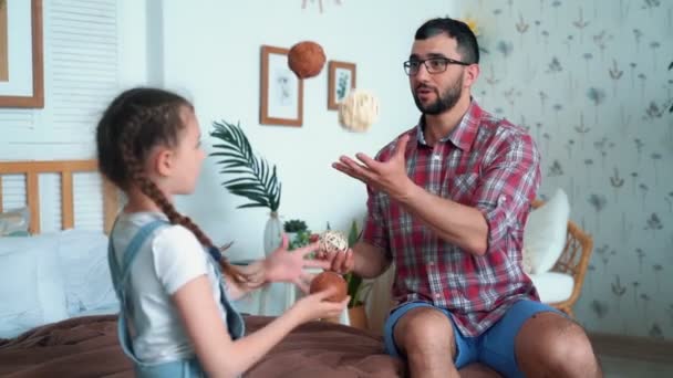 Pappa och dotter sitter på sängen och försöker jonglera med bollar, slow motion — Stockvideo