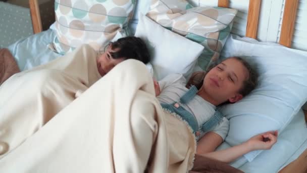 Две маленькие симпатичные девочки лежат в постели, улыбаются и смеются, замедленная съемка — стоковое видео