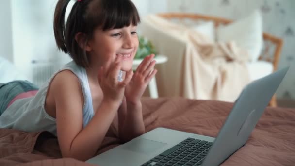 Little girl lying on bed, uses laptop, plays computer game, slow motion — Stock Video