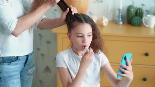 Menina bonito pinta os lábios com batom, enquanto a mãe penteia o cabelo, câmera lenta — Vídeo de Stock