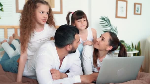 Счастливая семья, родители и две дочери смотрят кино на ноутбуке, замедленная съемка — стоковое видео