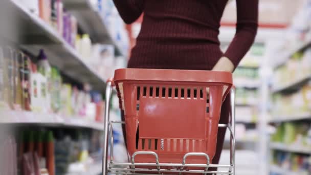 Primer plano de la mano de la mujer pone los productos en el carro cerca de los estantes en el supermercado — Vídeo de stock