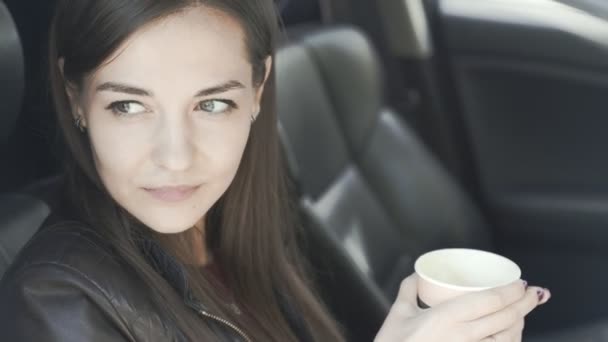 Mooie vrouw zit in de auto, drinkt koffie, kijkt uit raam en glimlacht — Stockvideo