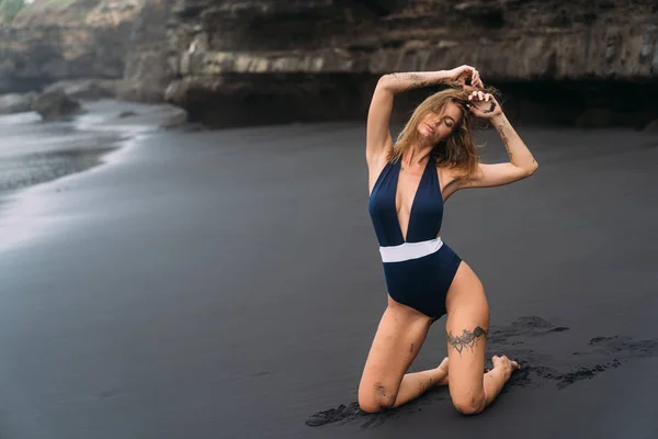 Ragazza sexy con grandi seni in costume da bagno blu rilassante in spiaggia con sabbia nera . — Foto Stock