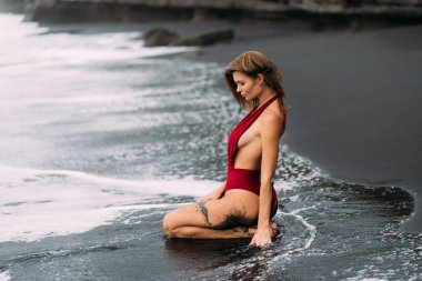 Kırmızı mayo büyük göğüsler ile seksi model siyah kum plajda pozlar.