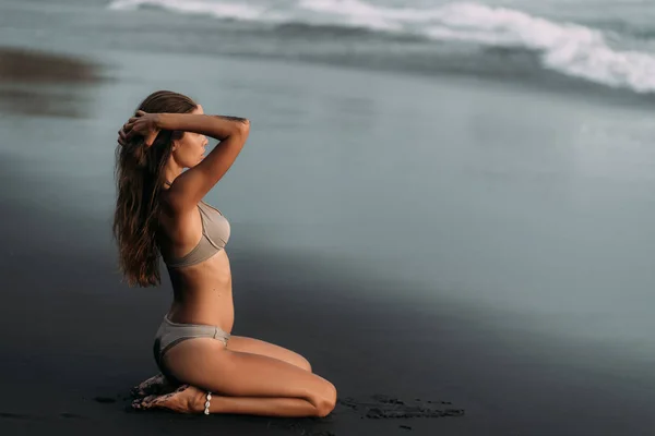 Сексуальна модель в бежевому купальнику спирається на пляж з чорним піском. Концепція подорожей — стокове фото