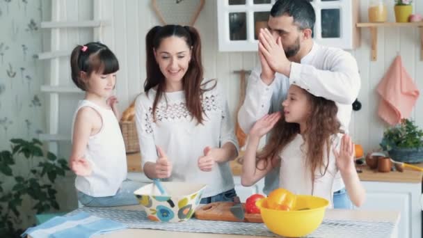 Батьки і дві доньки готують на кухні, показують великий палець вгору, повільний рух — стокове відео