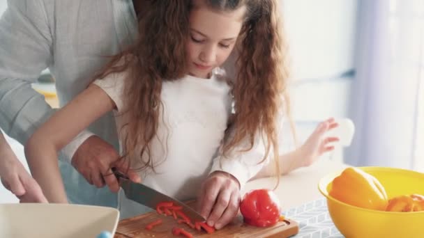 Yakın çekim, baba mutfak tahtasında biber keser, kızı ona yardımcı olur, yavaş hareket — Stok video