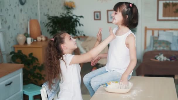 Niedliches Mädchen beschmiert Schwester Gesicht mit Mehl, haben Spaß in der Küche, Zeitlupe — Stockvideo