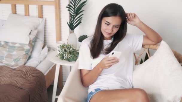 Belle fille est assise dans une chaise de paille et utilise le téléphone pour faire du shopping en ligne, au ralenti — Video