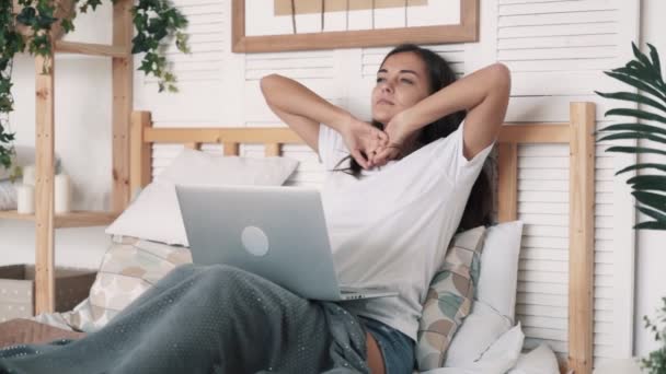 Femme fatiguée s'assoit sur le lit, utilise un ordinateur portable pour le travail à la maison et bâille, ralenti — Video