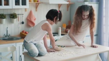 Mutfakta yemek pişiren iki küçük kız kardeş, masada unla çizim, yavaş çekim