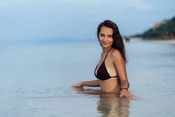 Felice abbronzata ragazza in costume da bagno si siede in mare e posa sulla spiaggia in vacanza — Foto Stock