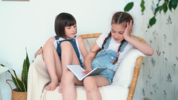 Dos niñas lindas se sienta en la silla, una de ellas cuenta cuento de hadas, cámara lenta — Vídeos de Stock