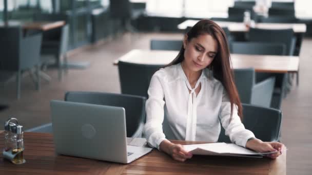 Femme d'affaires à l'heure du déjeuner dans un café regarde le menu, ordinateur portable sur la table, ralenti — Video