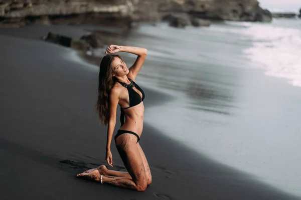运动女孩与性感的身体在黑色泳装休息在黑色沙滩 — 图库照片