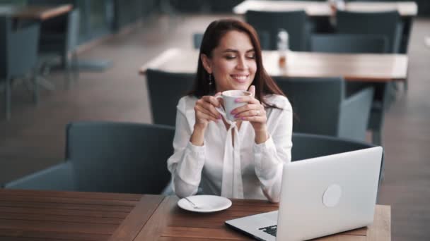 Piękna businesswoman ciesząc się kawą w kawiarni, laptop na stole, powolny ruch — Wideo stockowe