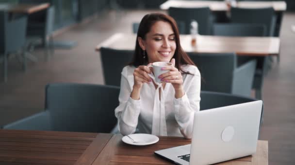 カフェでコーヒーを楽しむ美しいビジネスウーマン、テーブルの上のラップトップ、スローモーション — ストック動画