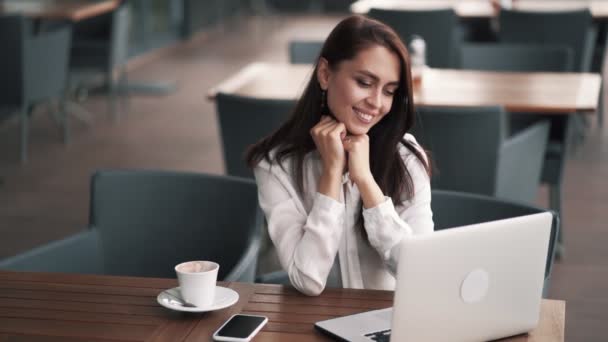 Üzletasszony ül kávézóban, mosolyogva, nézi a laptop képernyőjén, lassú mozgás — Stock videók