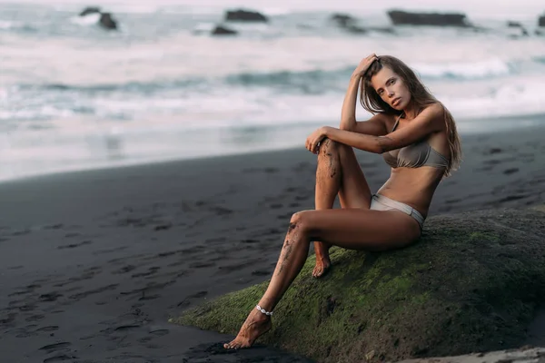Beautiful sexy model in beige colour swimsuit on black sand volcanic beach. — Stock Photo, Image