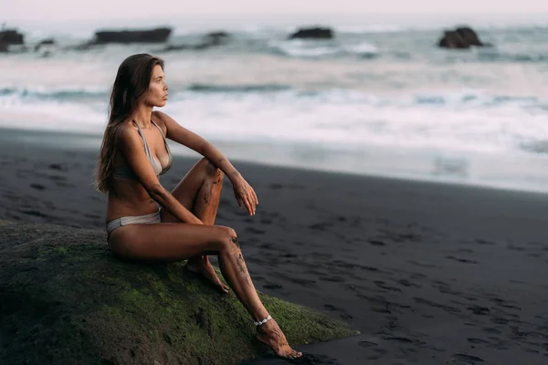 Aranyos szexi lány bézs fürdőruha nyugszik fekete vulkáni homok strand. — Stock Fotó