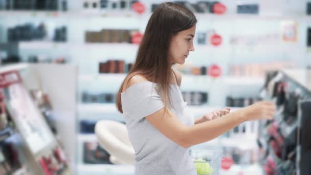 Chica bonita elige rímel en la tienda de cosméticos, se abre y huele, cámara lenta — Vídeos de Stock