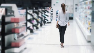 Backside görünümü, kozmetik mağazasında kız alışveriş, raflar arasında gitmek, yavaş hareket