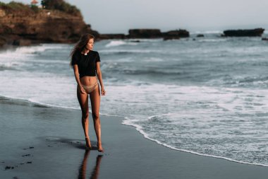 Gün batımı ışınları siyah kumlu plajda siyah t-shirt ve mayo kız