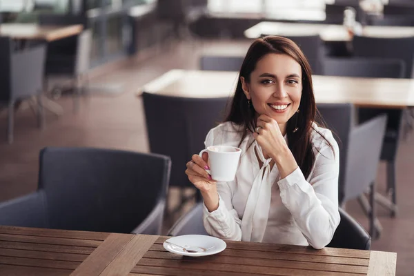 Beautiful business woman drinks coffee in cafe, lunches in cafe during her break