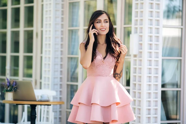 Hermosa chica en vestido rosa hablando por teléfono en la cafetería de la calle, concepto freelancer — Foto de Stock